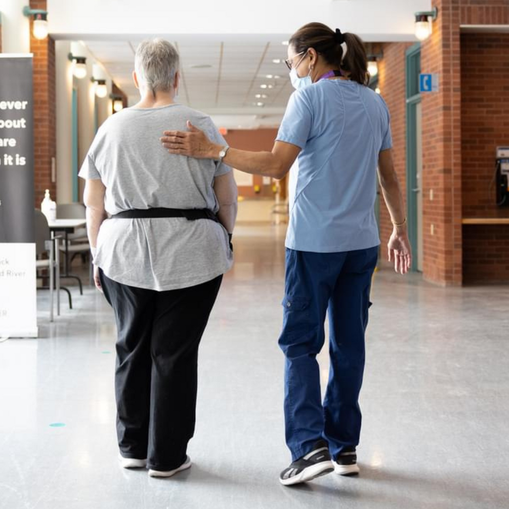 A healthcare worker walks down the hall at the Freeport Campus alongside an elderly patient with her hand on her back