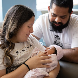 Image of Two parents look down at their infant, who is being cradled by their mother.