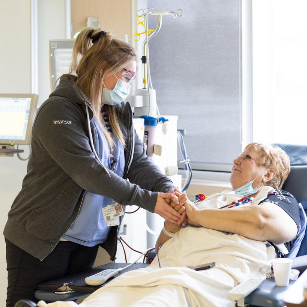 A healthcare worker clasps hands with a dialysis patient during treatment for support.