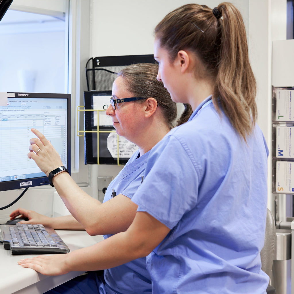 A nurse trains a medical student on a computer application at the ICU nursing station.